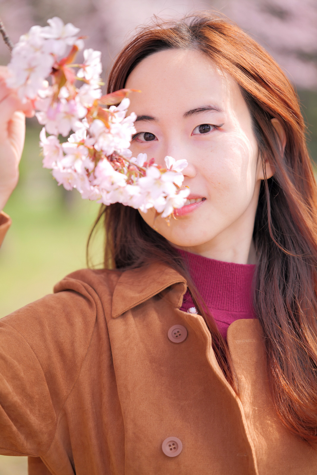 桜の花越しに見つめる女性モデル・クレアのクローズアップポートレート