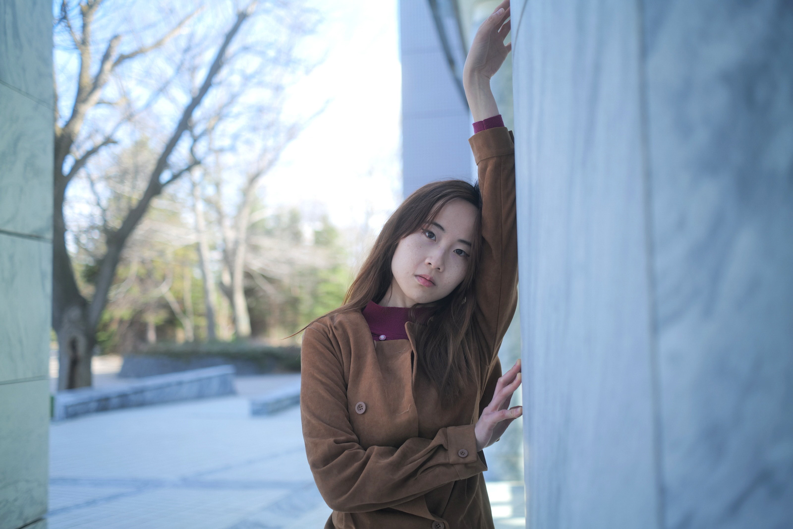 建物の壁にもたれ腕を上げる女性モデル・クレアのクールトーンポートレート